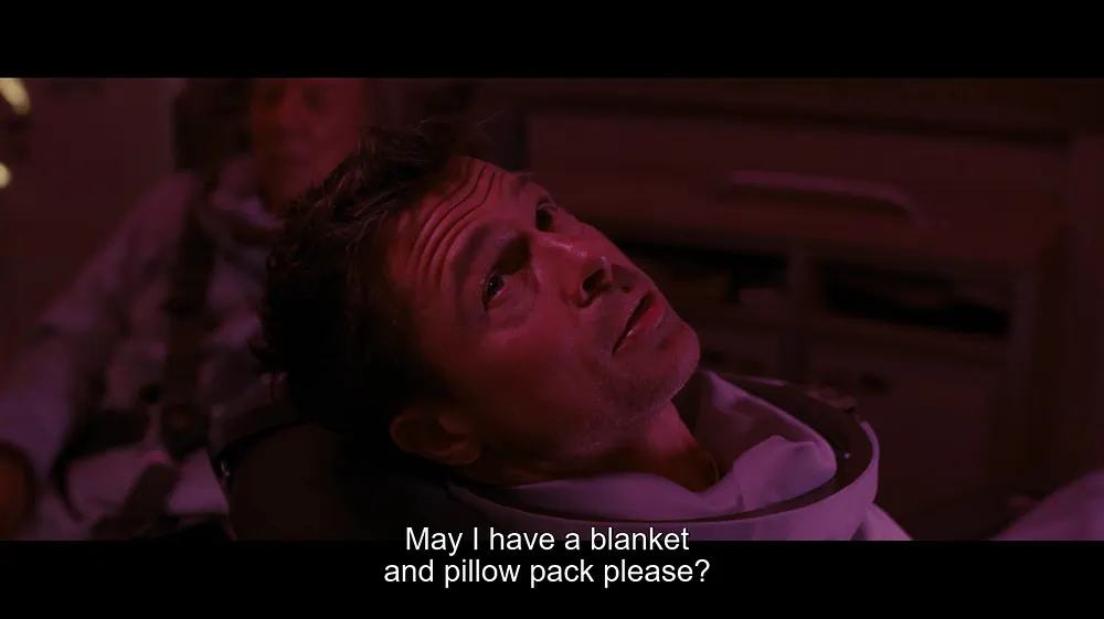 Movie still from Ad Astra (2019) showing Brad Pitt's character lying down in what appears to be a spacecraft seat, bathed in pink and purple lighting. He looks upward with a concerned expression. Subtitles read: 'May I have a blanket and pillow pack please?